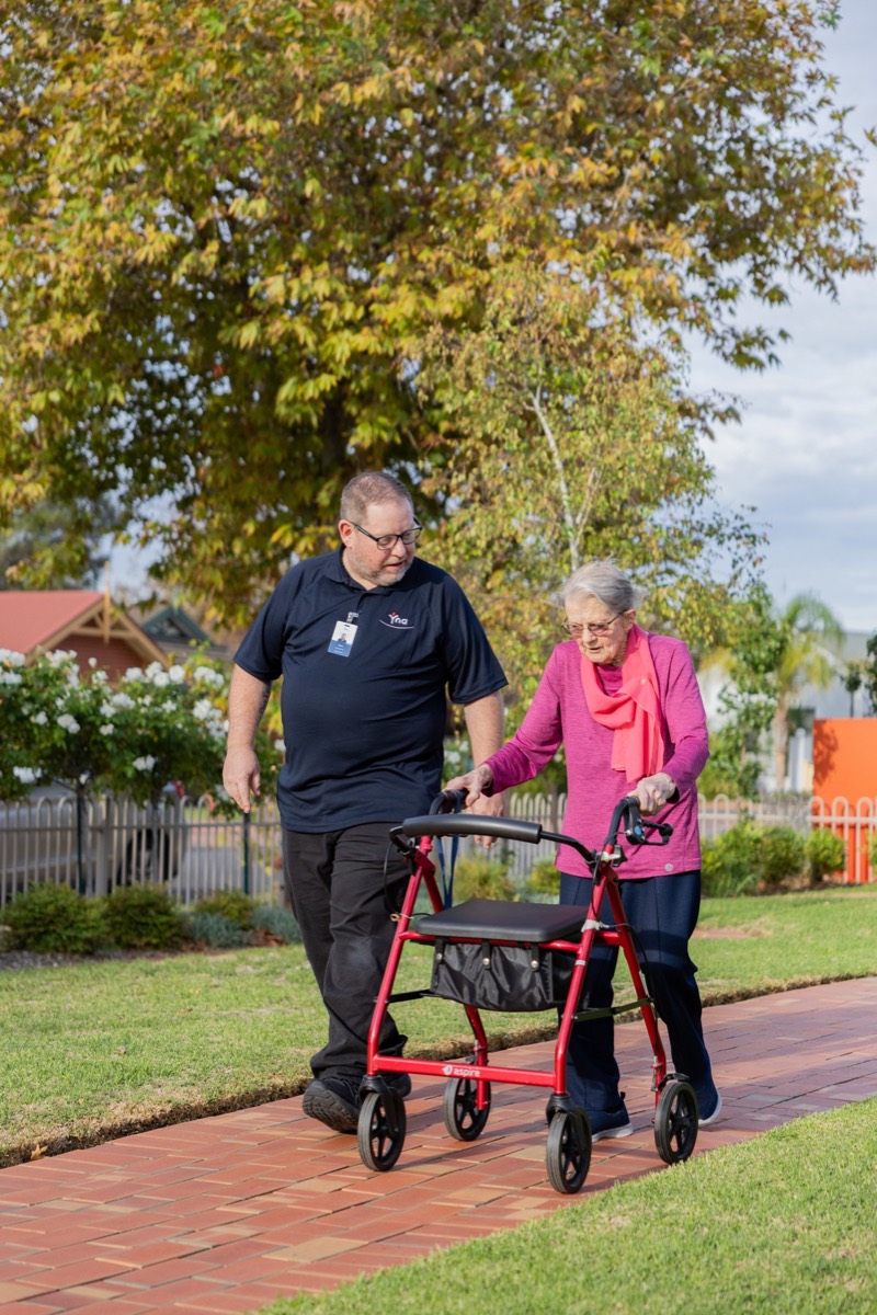 A support worker walking with a resident along a garden path